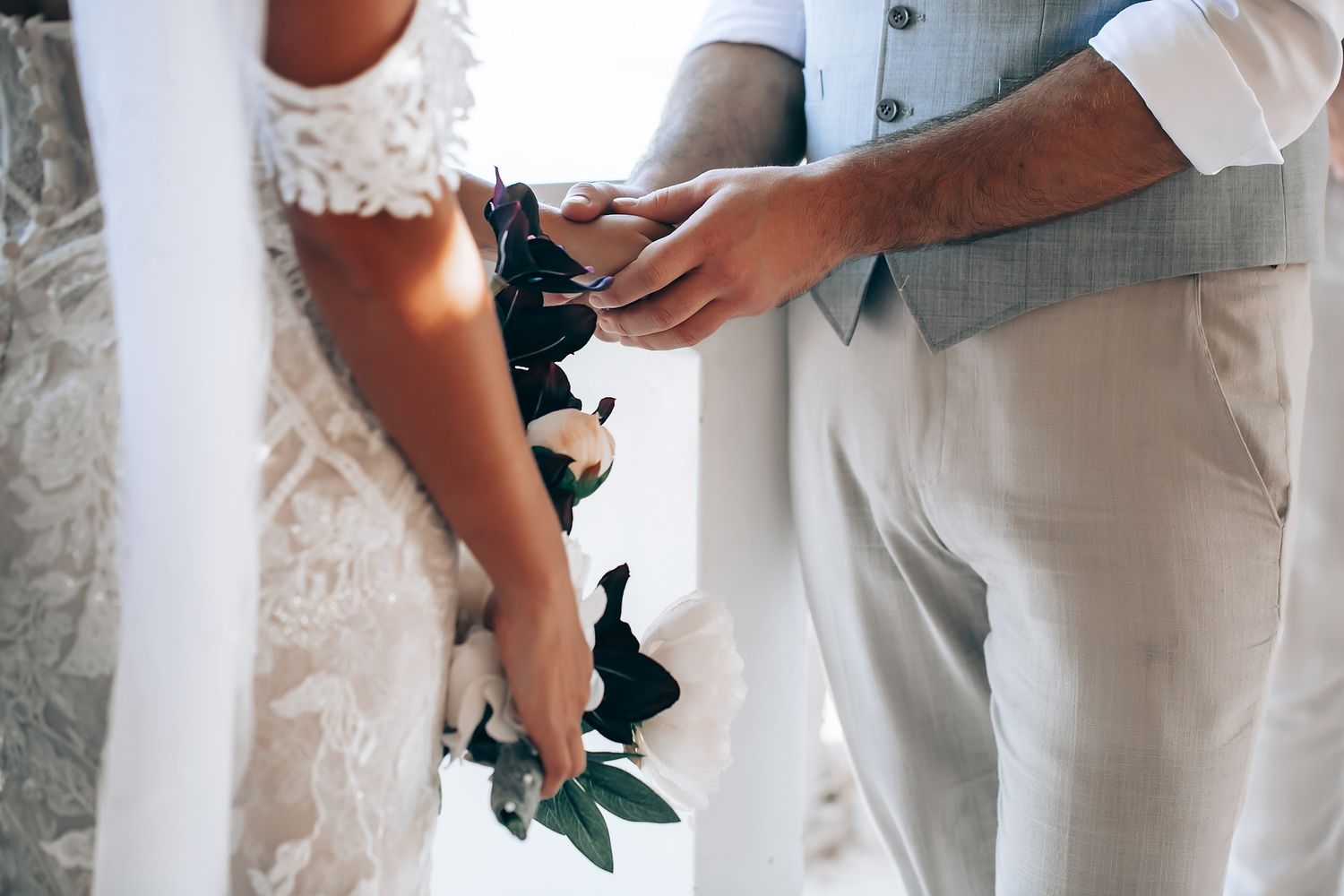 Close-up details of wedding party members in white formal attire holding bouquets.