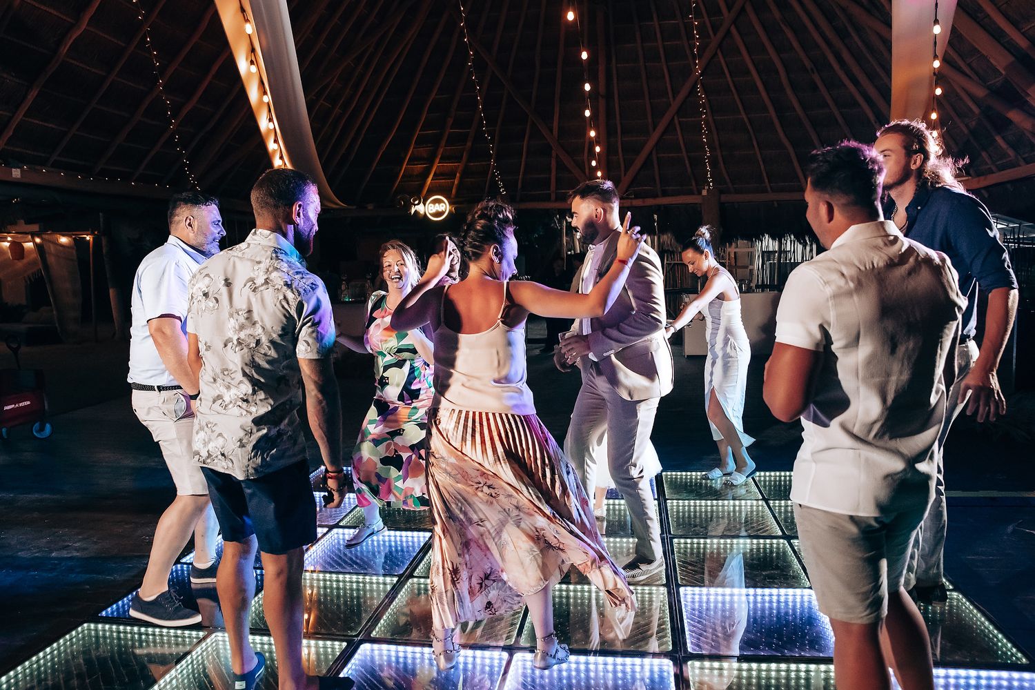 People dance and socialize on an illuminated dance floor at a nighttime party event.