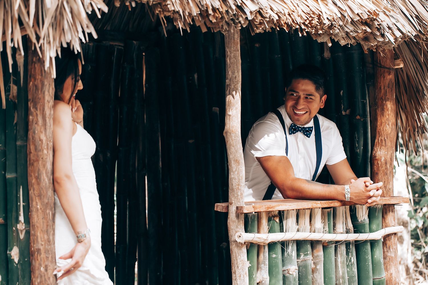 A rustic bamboo hut with a thatched roof serves as a romantic setting for a wedding photo shoot.