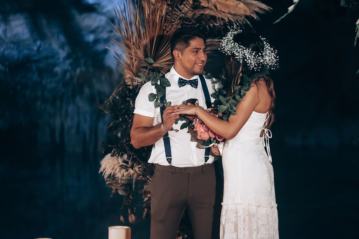A couple in formal wedding attire exchange rings during an outdoor ceremony in a scenic garden setting.