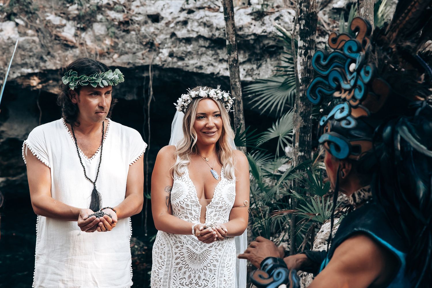 Group dressed in white stands together against a backdrop of dark rocks and tropical foliage.