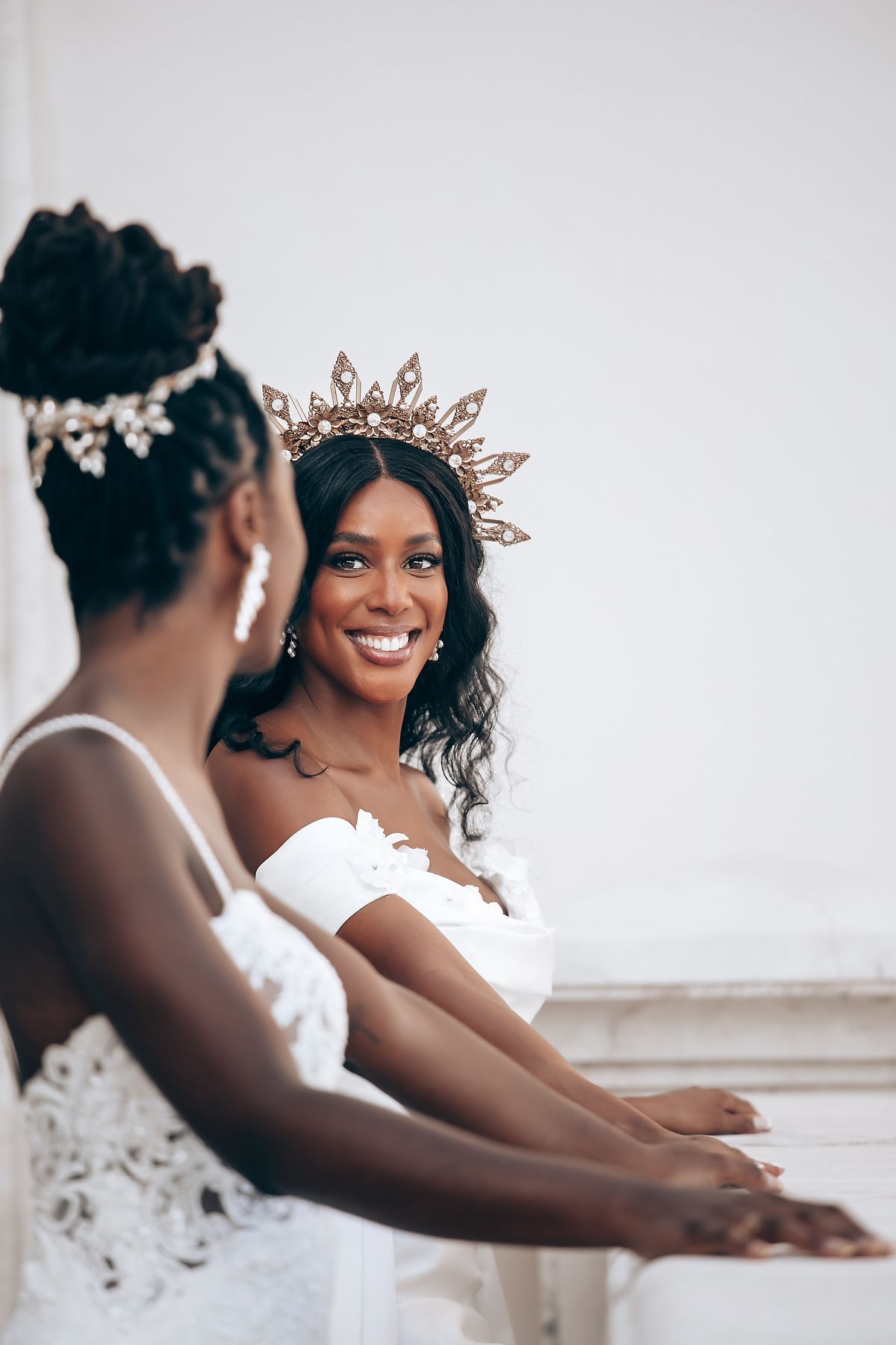 Elegant bridal party wearing delicate crowns and white gowns pose together.