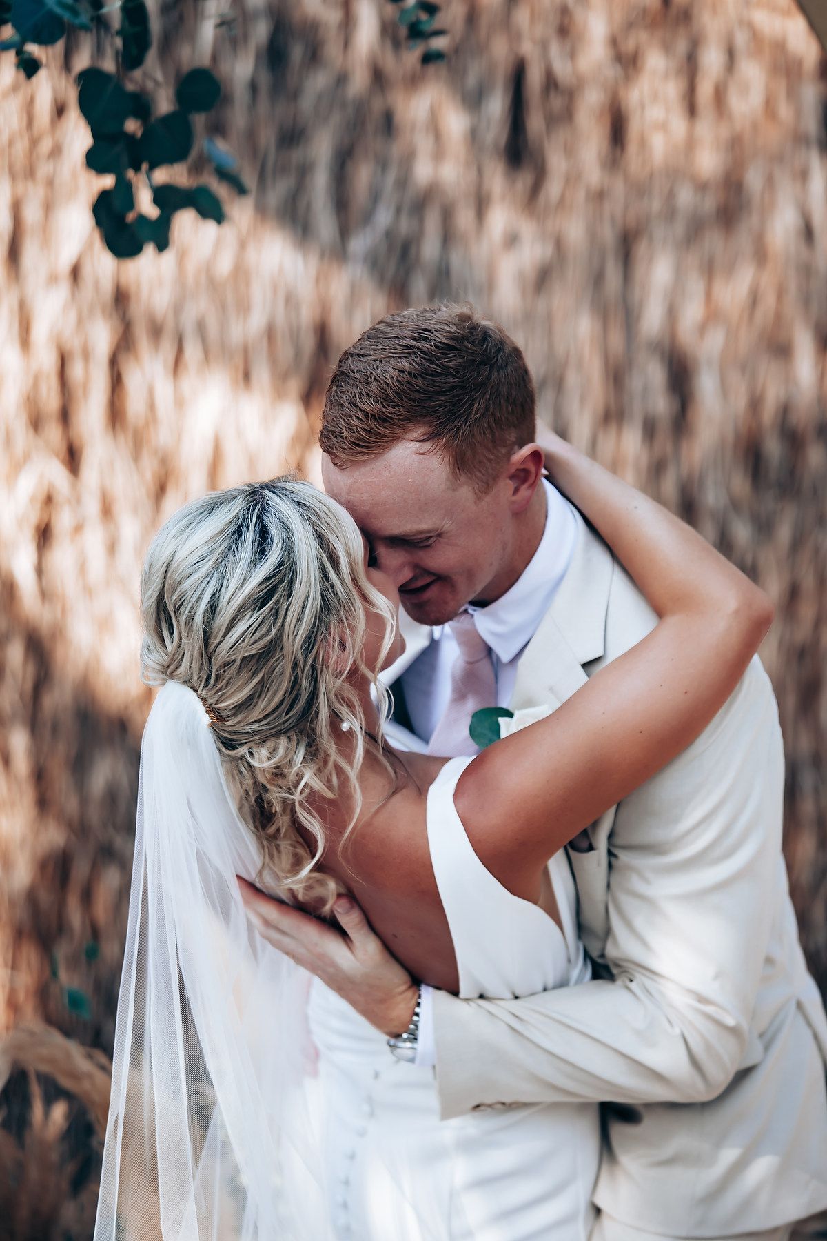 Newlyweds share an intimate moment against a rustic outdoor backdrop.