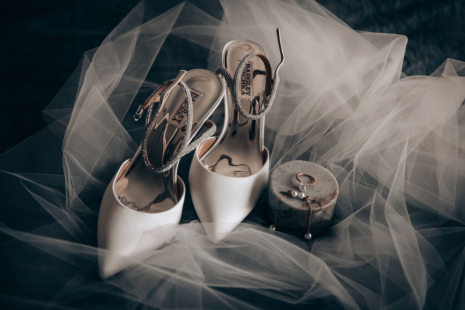 White bridal shoes and delicate tulle veil arranged on dark background.