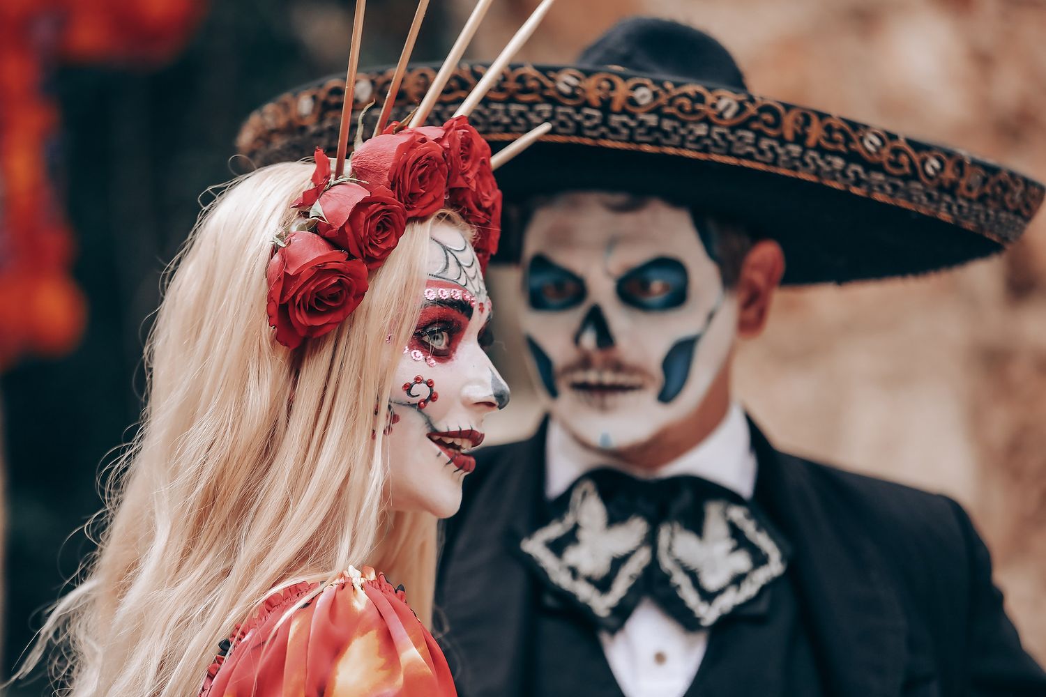 Close up of couple with sugar skull makeup wearing formal attire and floral accessories.