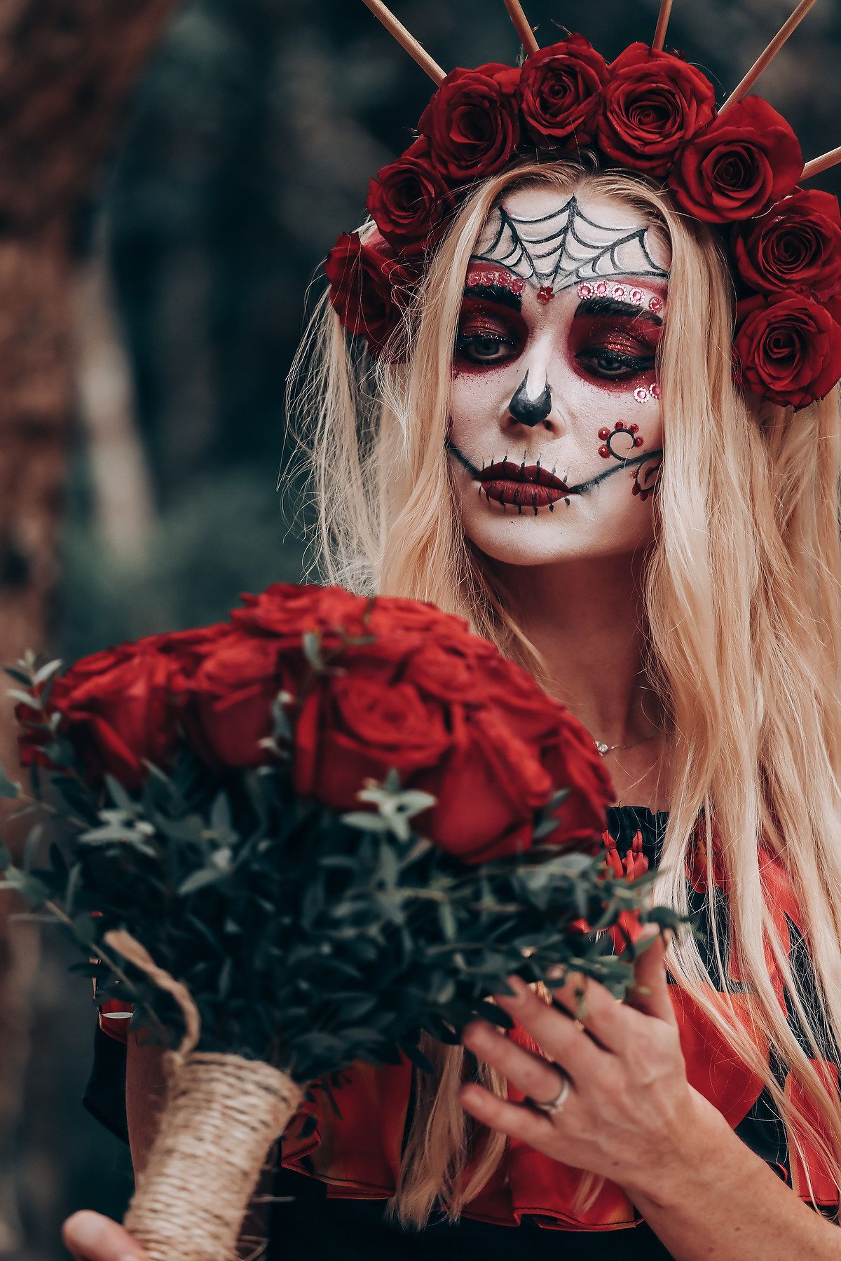 Day of the Dead themed portrait with red roses and sugar skull makeup against a dark background.