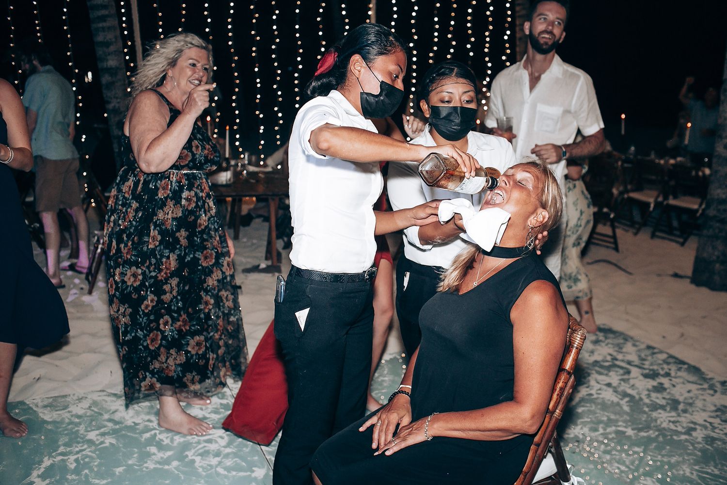 Wedding guests dancing and celebrating at a nighttime beach reception with fairy lights.