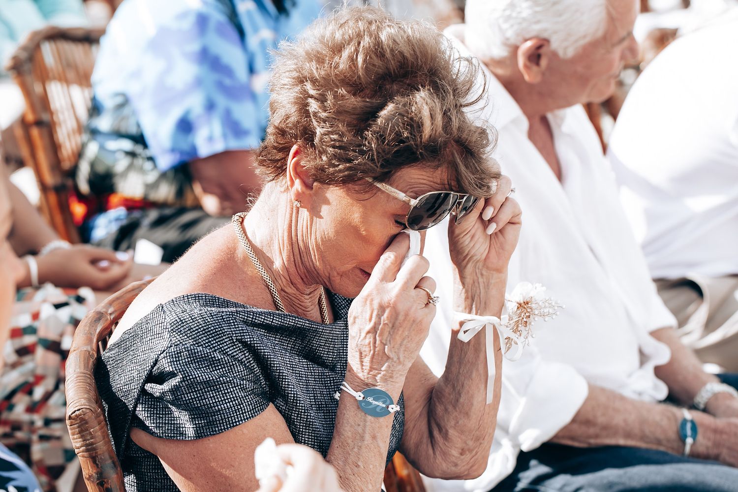 Wedding guests react emotionally during ceremony with tears and tissues on a sunny day.