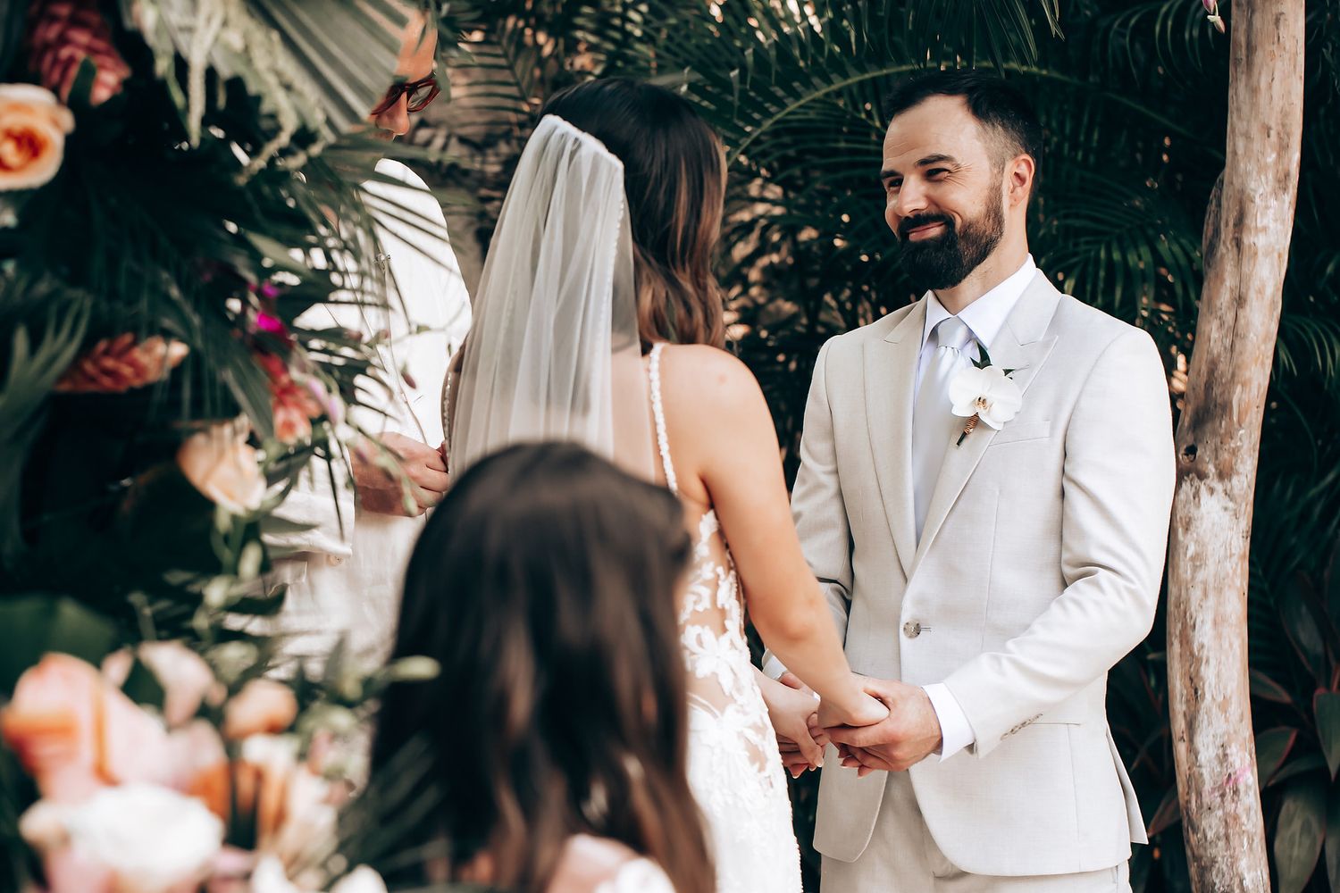 Wedding celebration with guests in white and neutral attire mingling in a tropical garden setting.