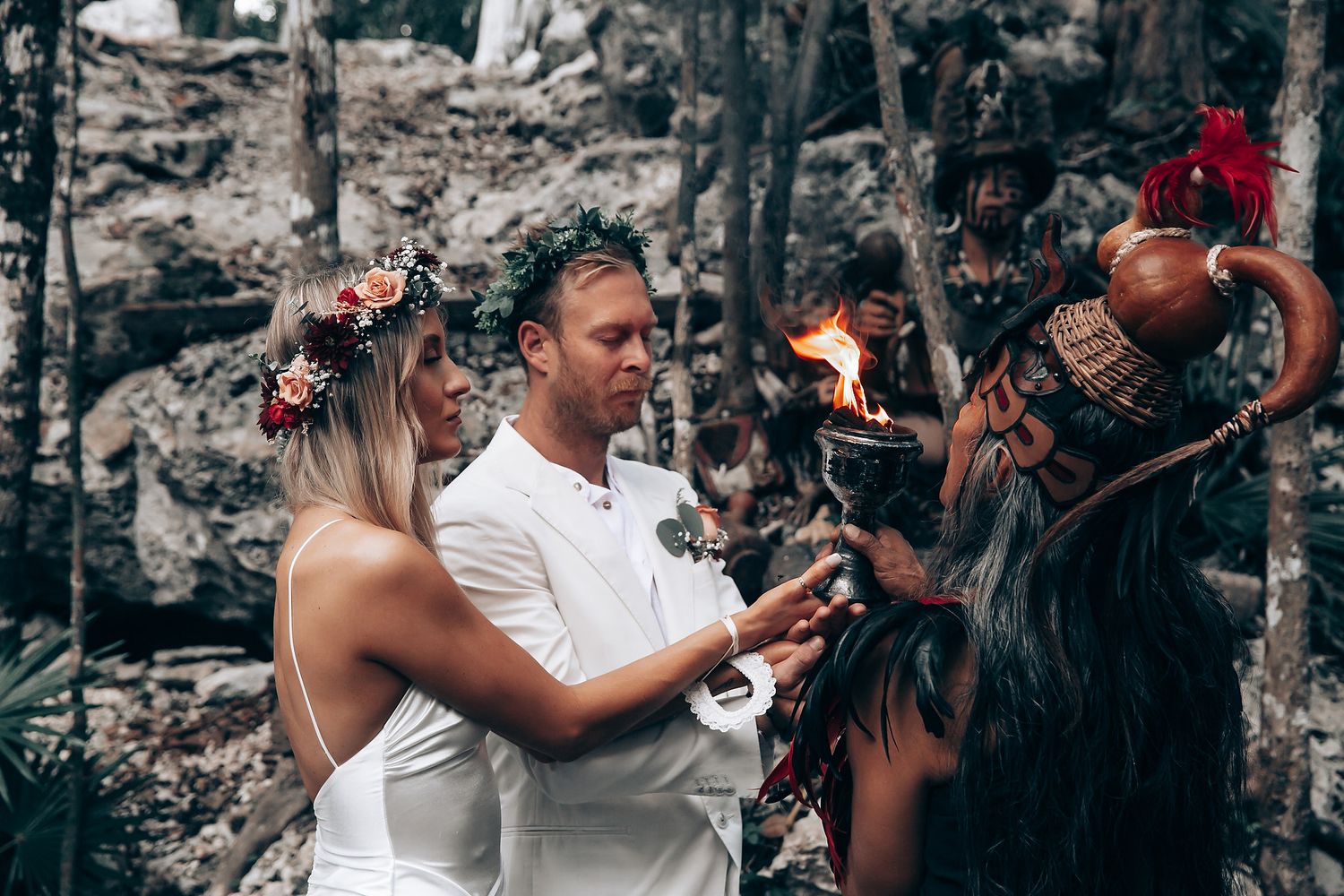 Traditional Mayan ceremony performers conduct a ritual with fire and decorative elements in a forest setting.