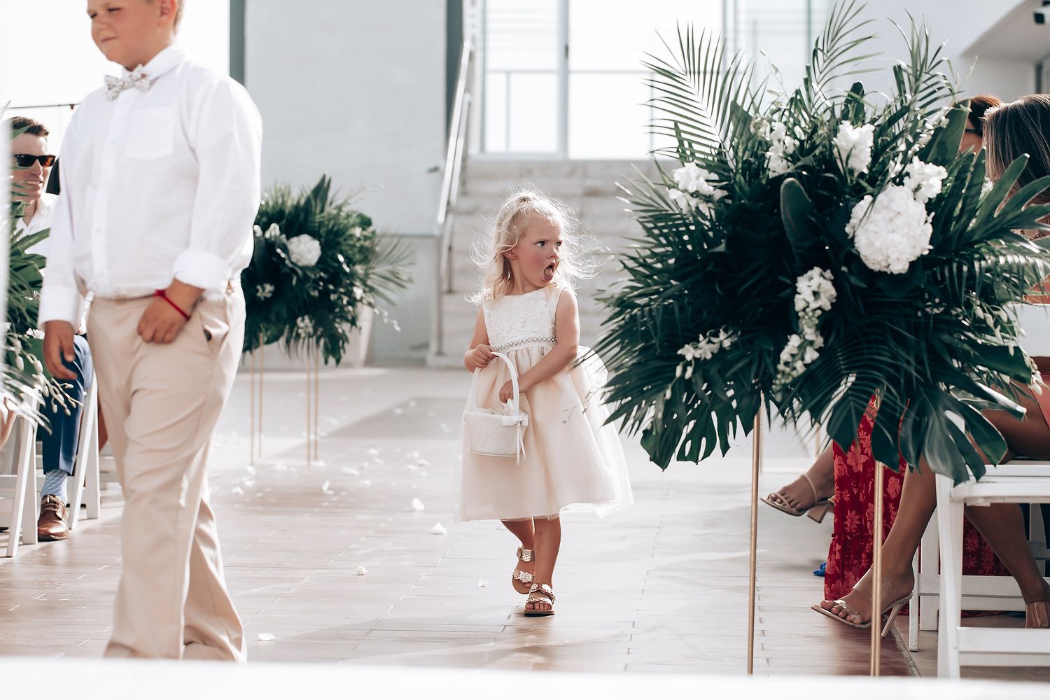 Wedding party in white and beige attire dancing together at an elegant indoor venue with tropical decor.