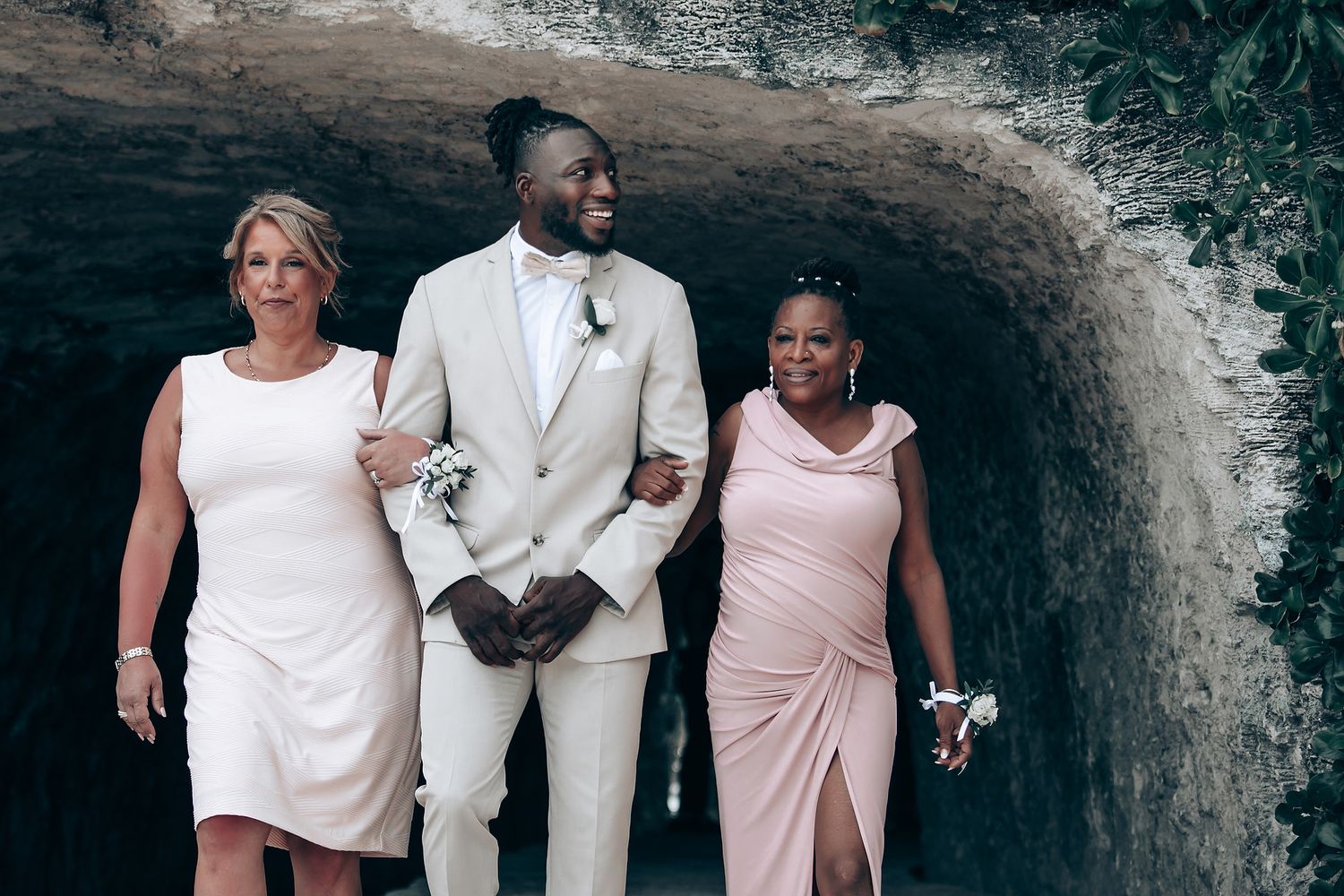 Wedding attendants in formal attire pose together in a stone archway.