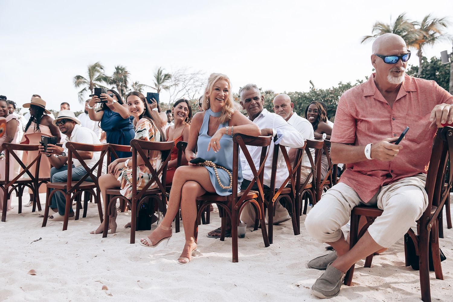 Guests seated in wooden chairs at outdoor beach wedding ceremony.