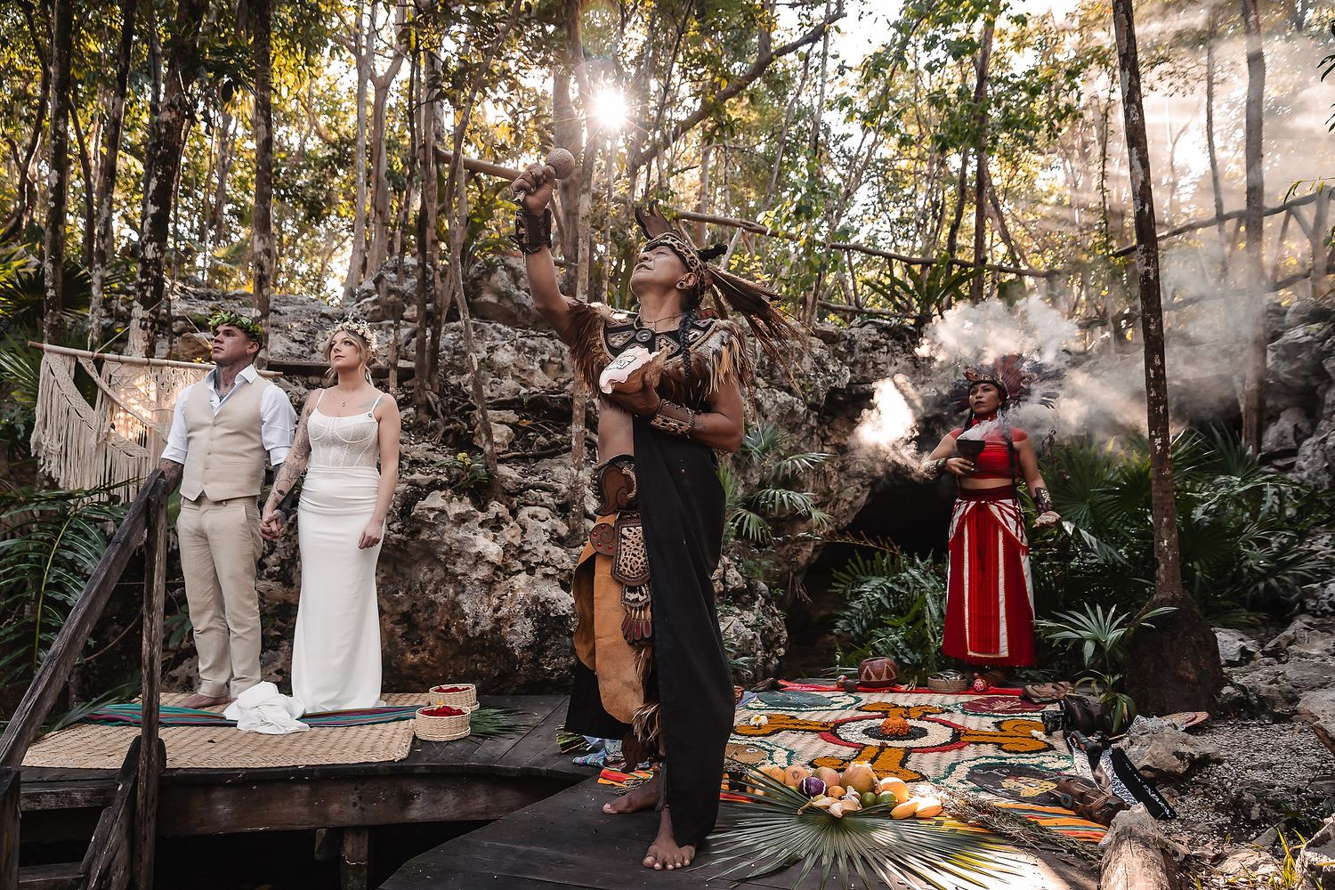 Mayan shaman performs ritual with smoke during jungle wedding ceremony beside colorful ceremonial altar.