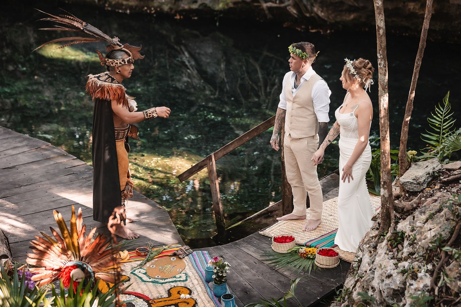 Mayan shaman officiating a boho wedding ceremony for a couple at a lush cenote in Mexico.