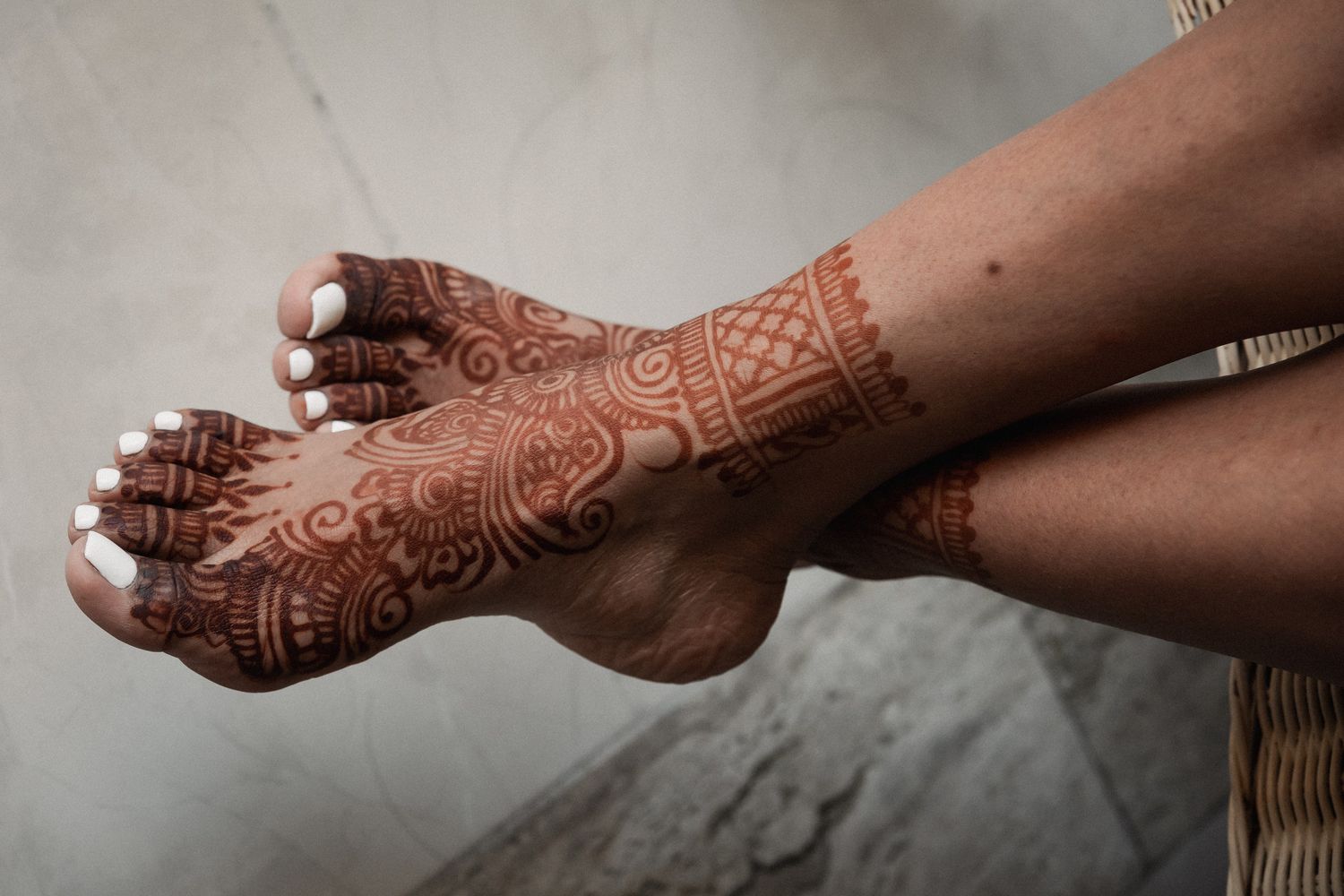 Close-up of intricate bridal mehndi henna designs on a woman's feet and ankles with white nail polish.