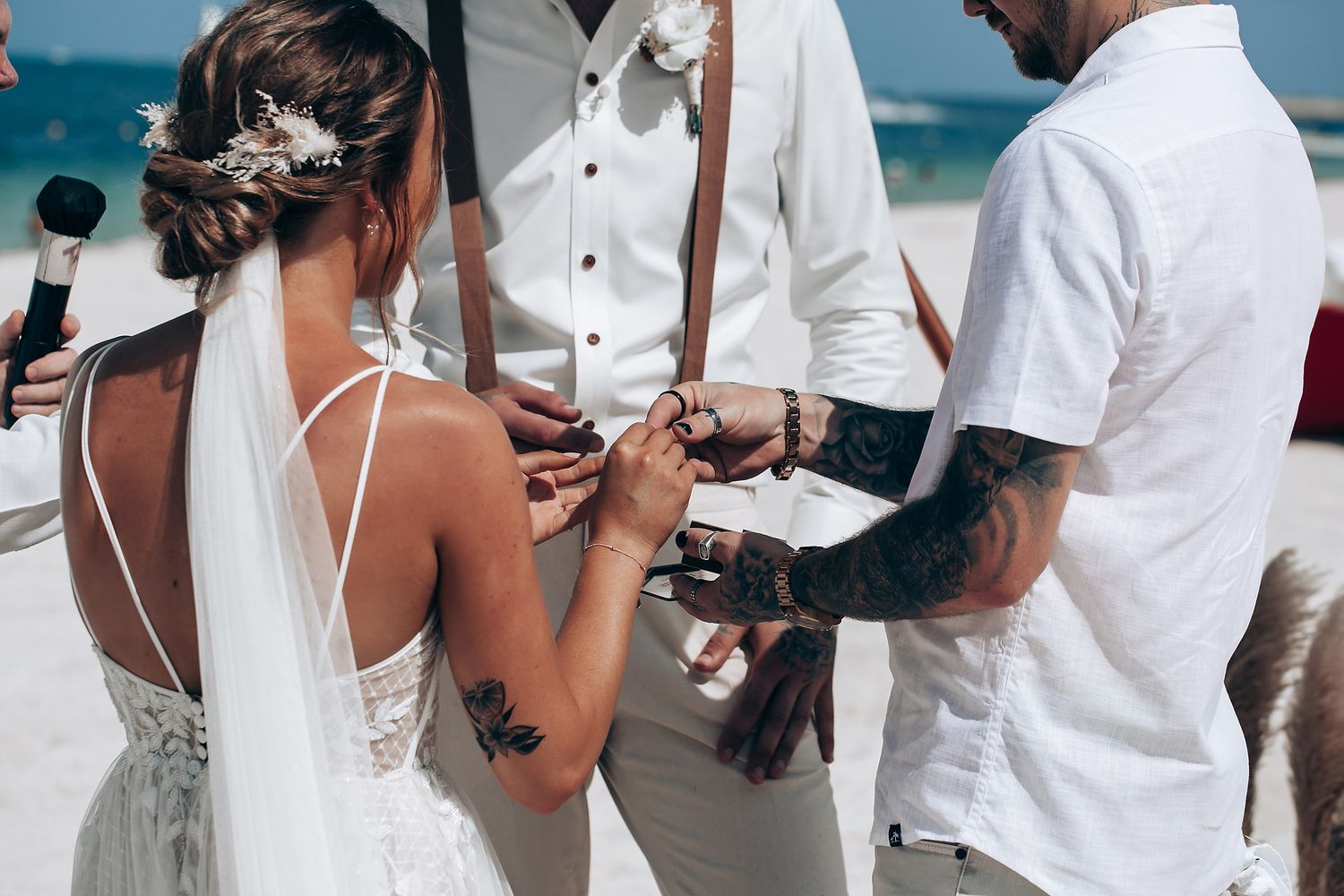 Wedding guests gathered on a beach with white attire and ocean backdrop.