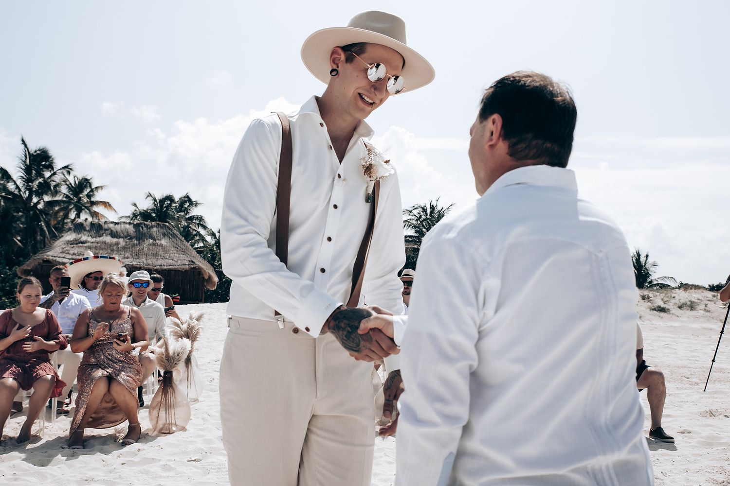 A beachside wedding ceremony with guests in white attire and palm trees in the background.