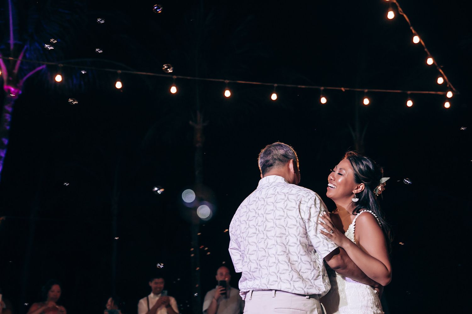 Evening wedding reception with string lights creating romantic ambiance on dark beach setting.