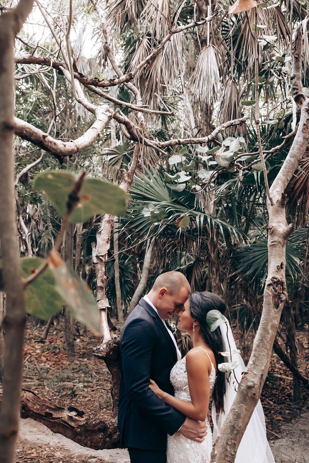 Newlyweds share an intimate moment among palm trees in a tropical forest setting.