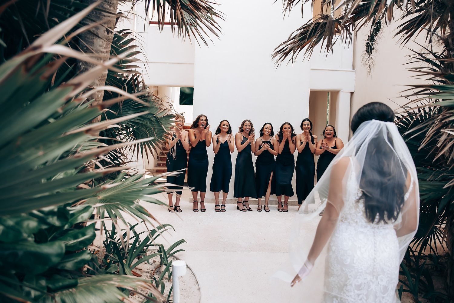 Wedding party in black and white attire standing together under palm trees at a tropical destination.