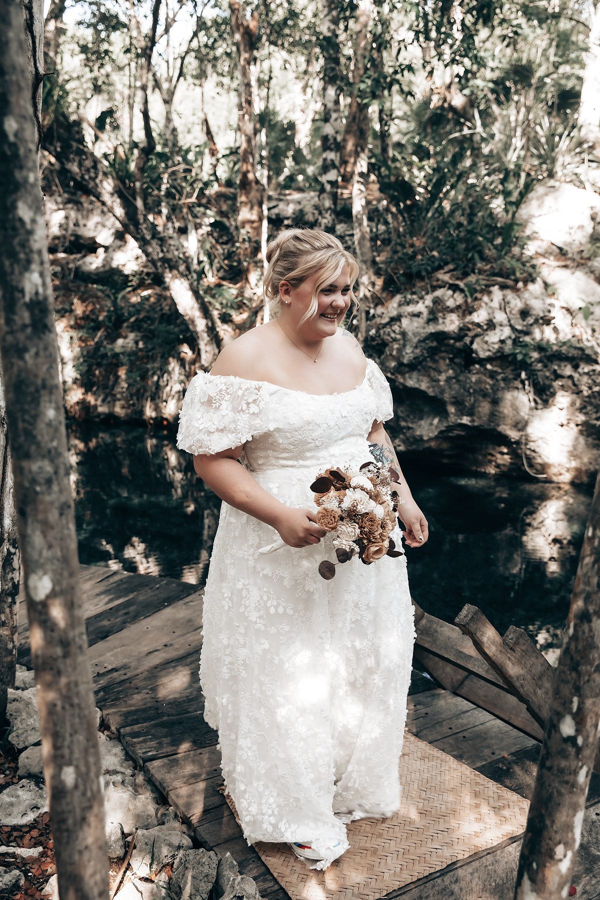 A person dressed in traditional indigenous attire standing on a wooden platform in a forested setting.