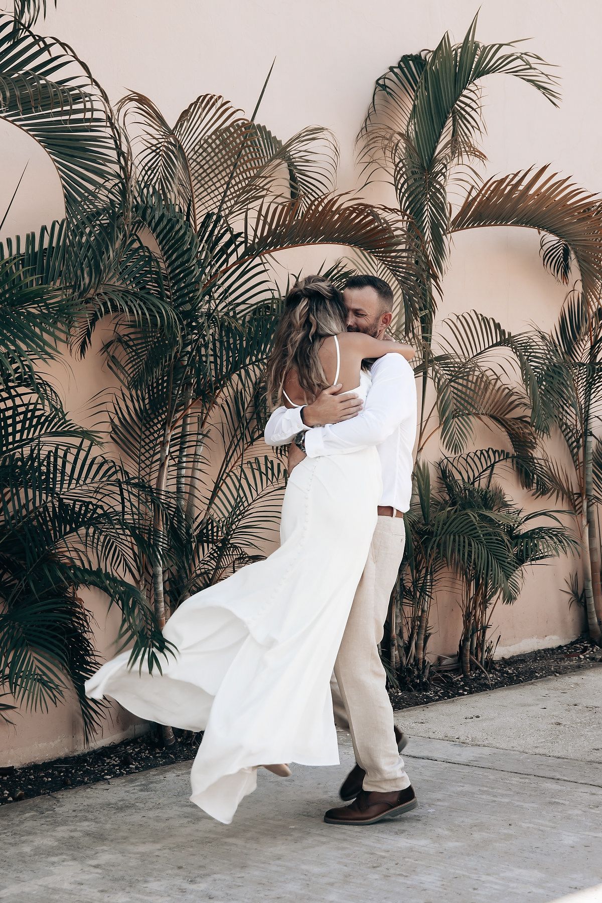 A bride and groom embrace in an outdoor wedding setting with palm trees in the background.