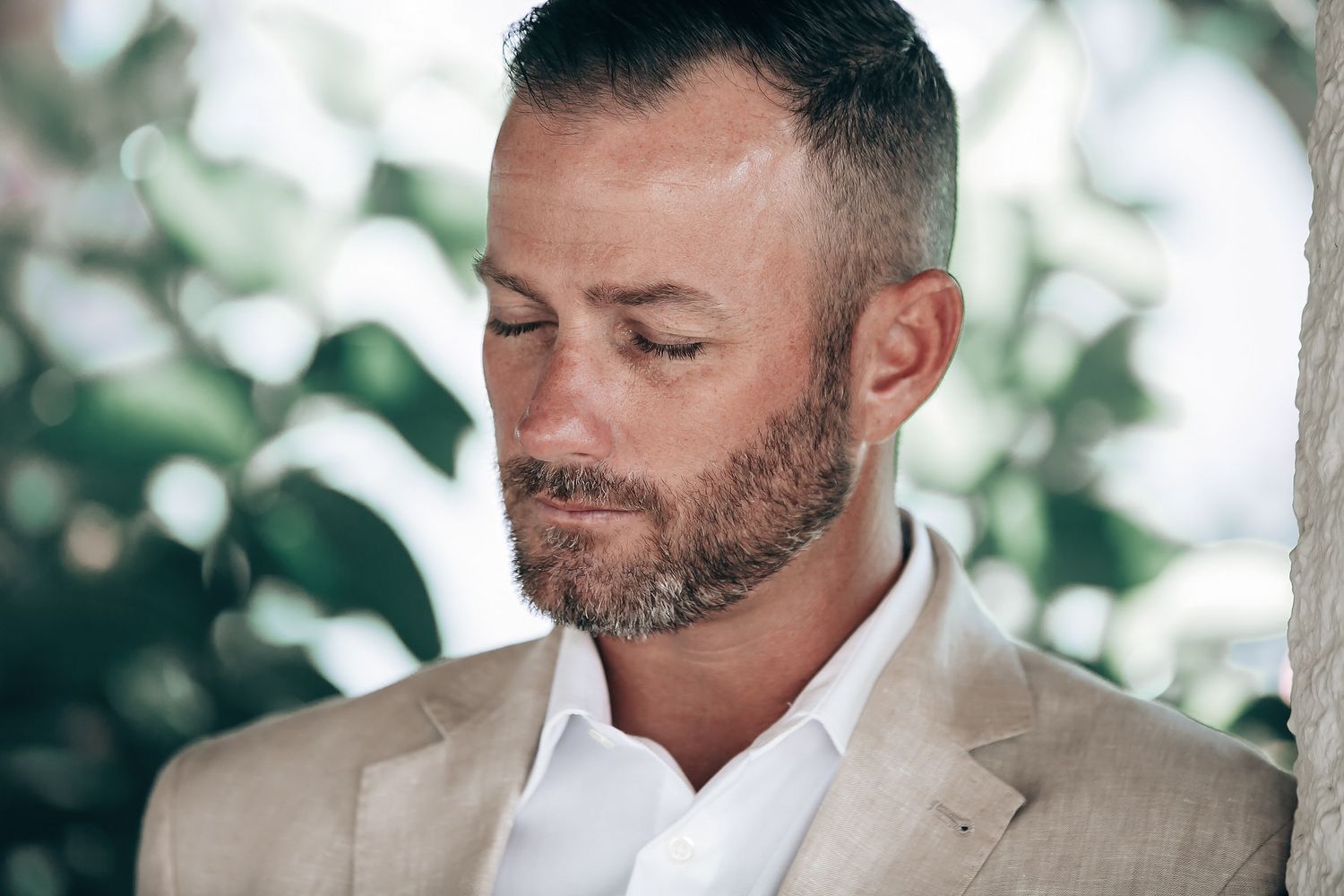 A man with a beard is standing in a garden and looking away.