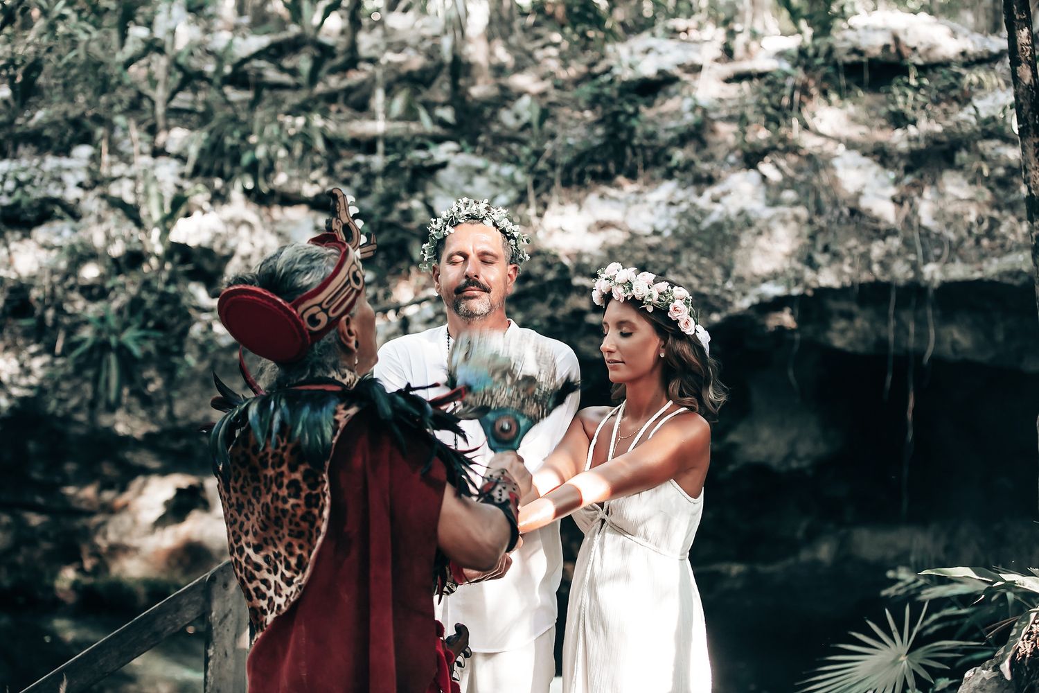A couple stands together in a lush, tropical forest setting, surrounded by various decorations and elements.