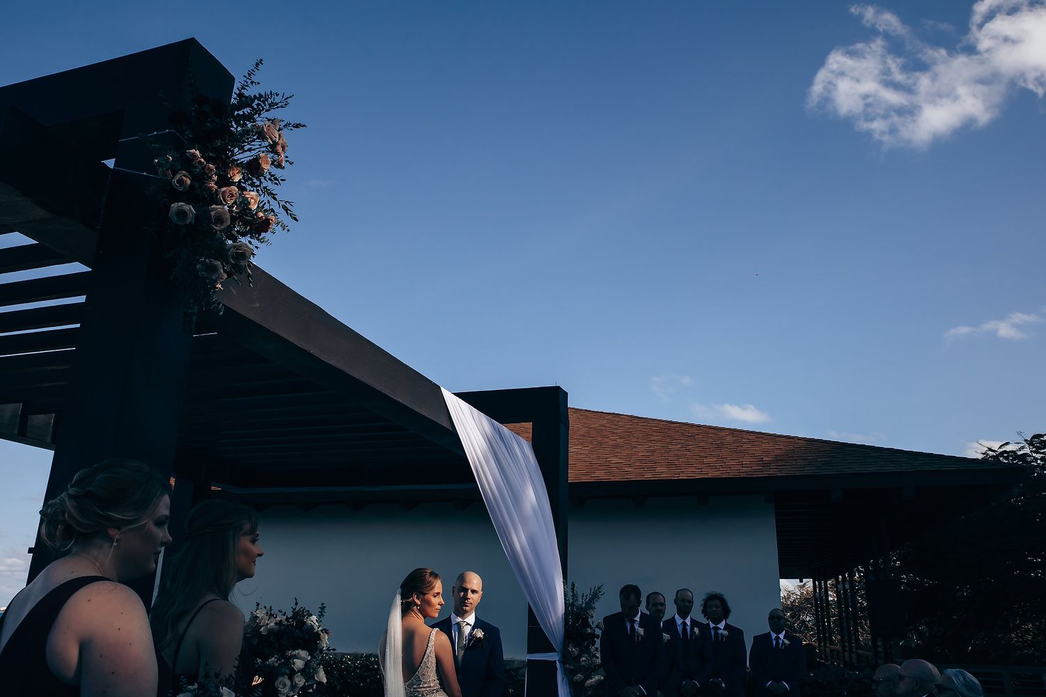 A couple stands together in a romantic outdoor wedding setting with a decorative arch and flowers.