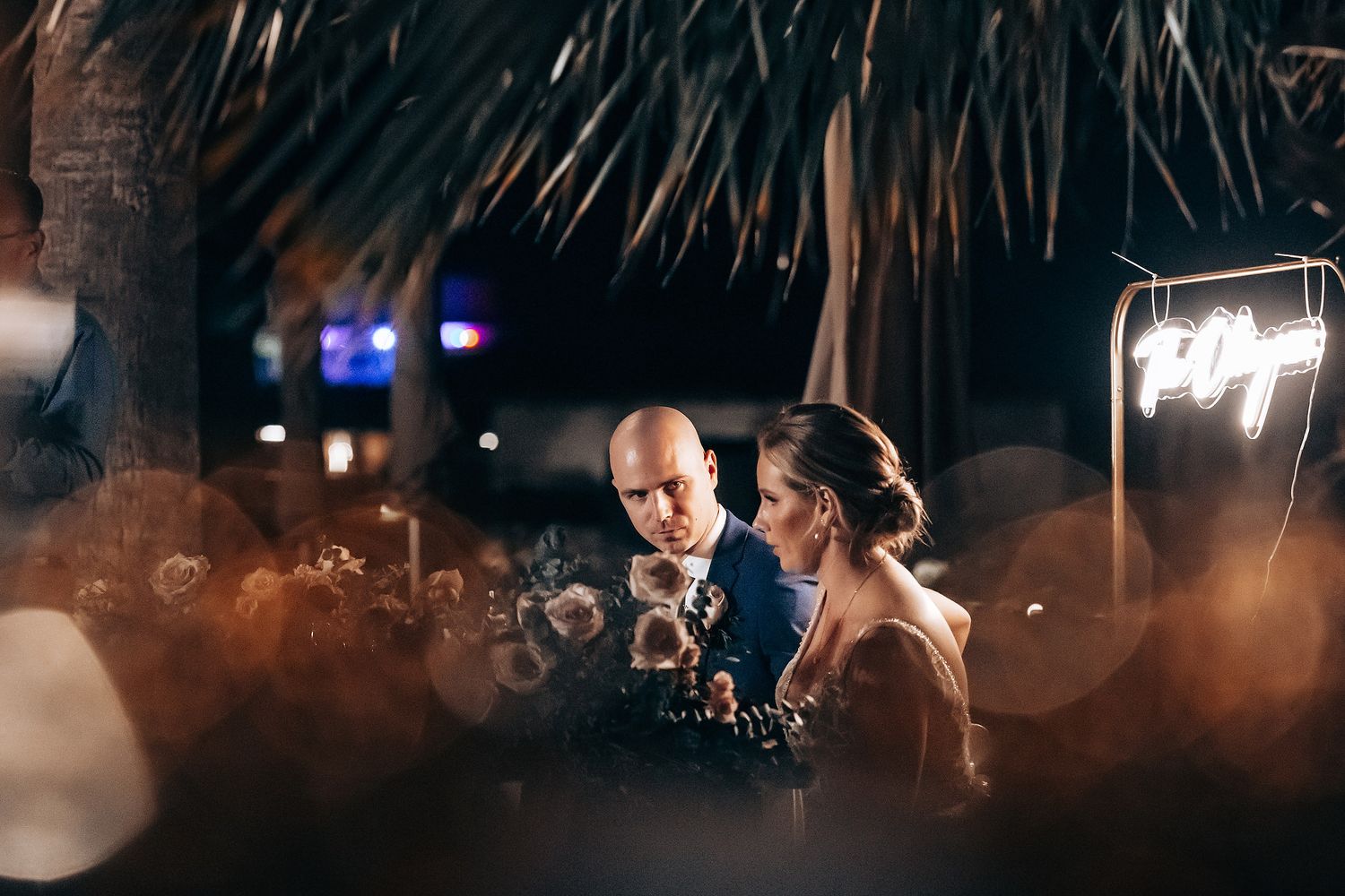 A bride and groom share a tender moment under twinkling lights at night.