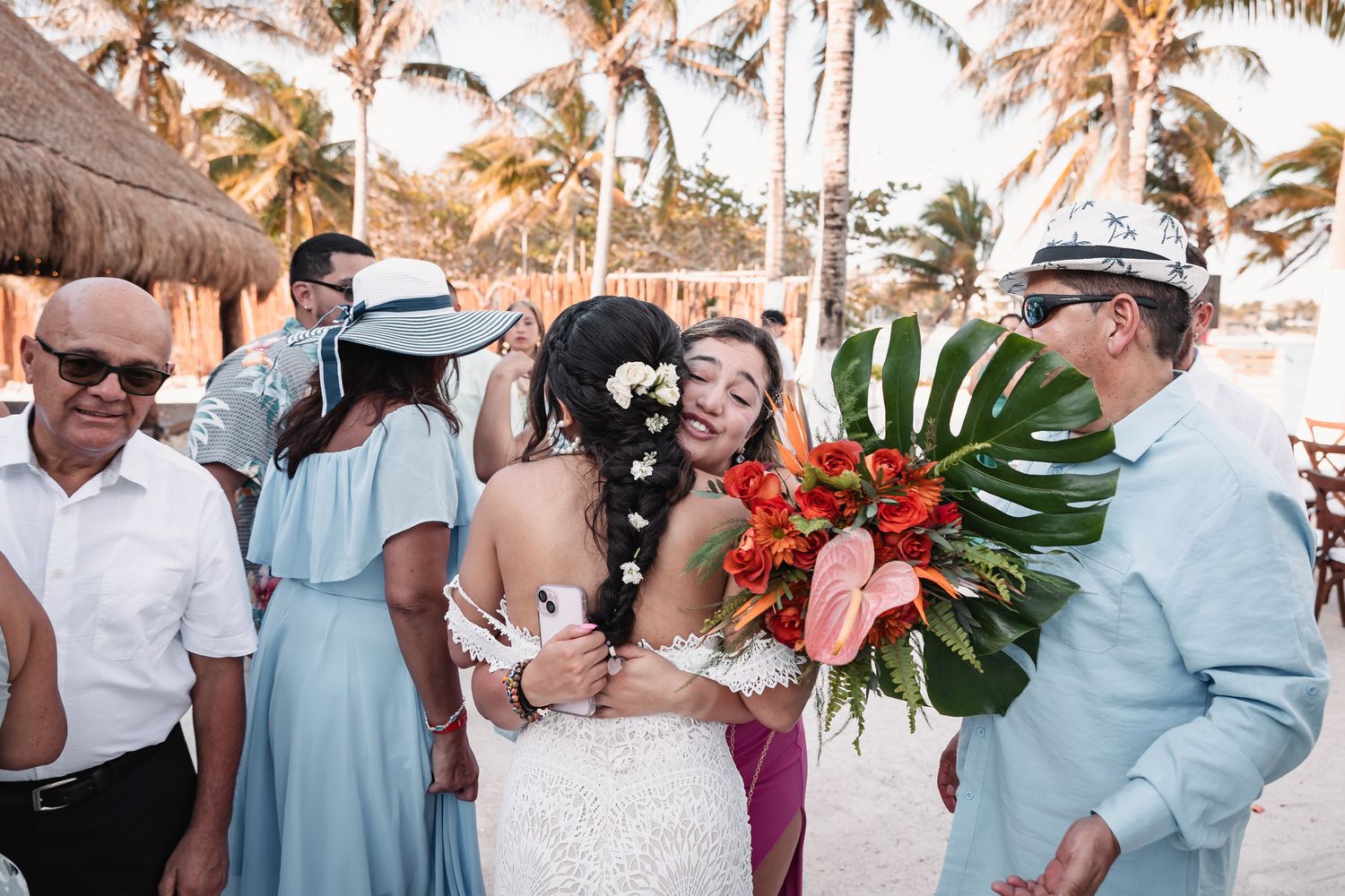 Bride hugs guest while holding tropical floral bouquet after beach wedding ceremony.