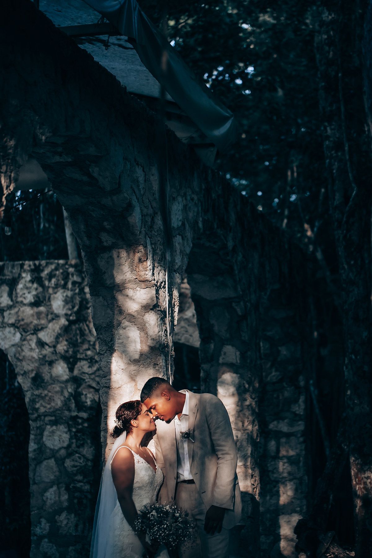 Romantic couple shares intimate moments in a rustic stone archway setting with dramatic lighting and shadows.