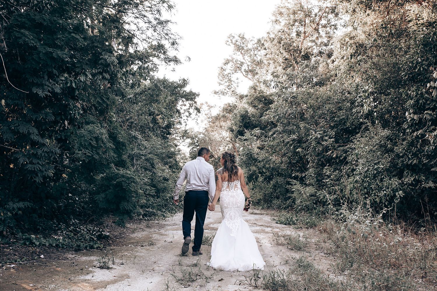 Romantic wedding couple walking down a sunlit forest path.