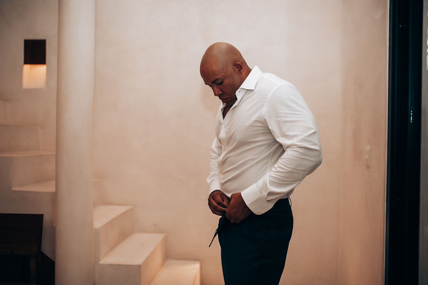 Silhouette of person in white shirt standing against minimalist white interior with stairs.