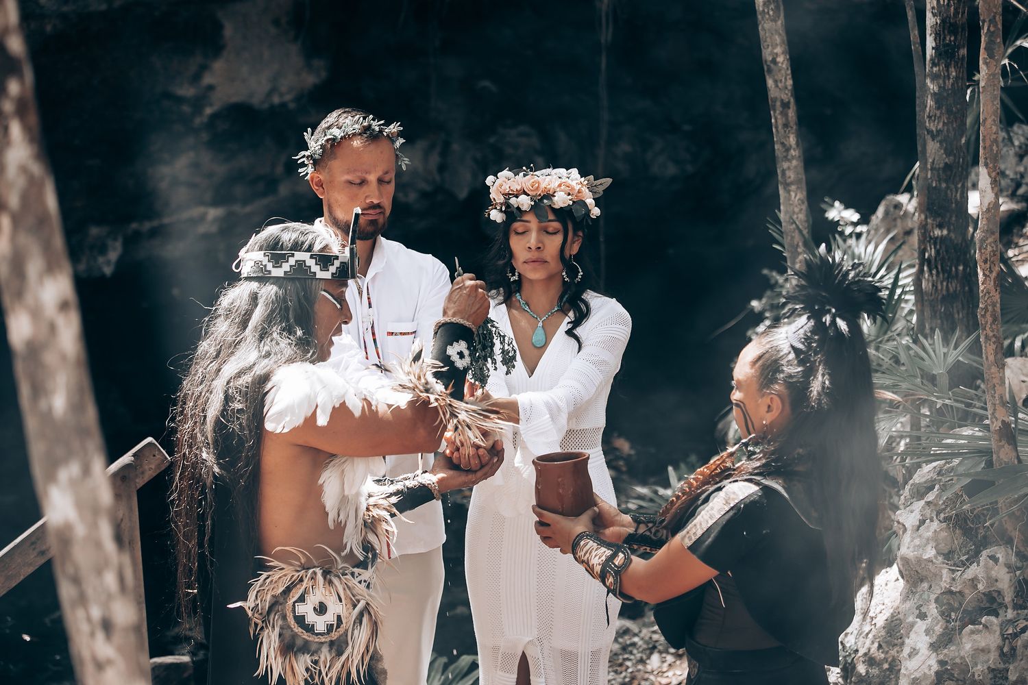 Wedding ceremony in a wooded area with guests gathered around a couple in white attire.