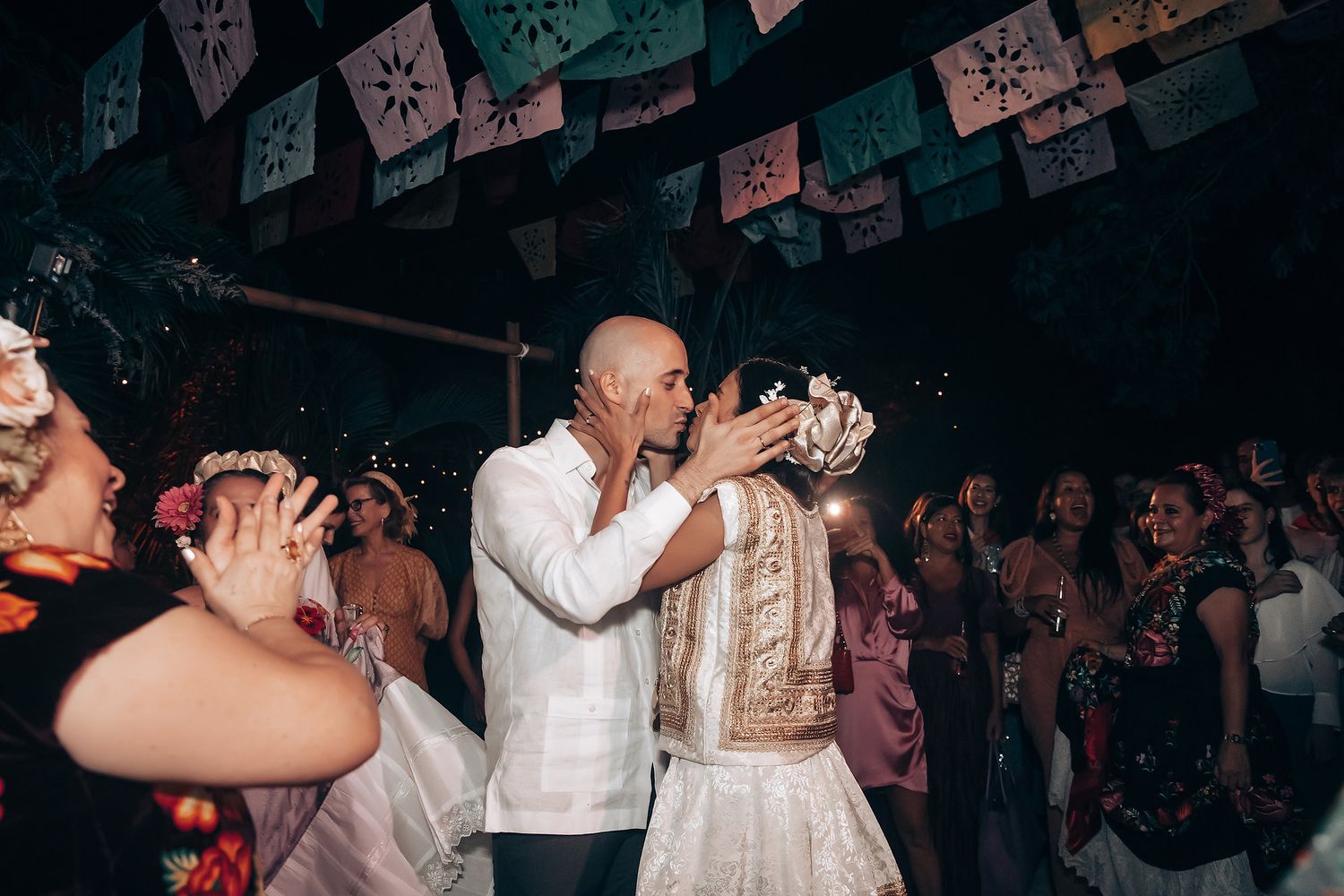 A celebratory moment at a wedding reception with guests dancing under papel picado decorations.