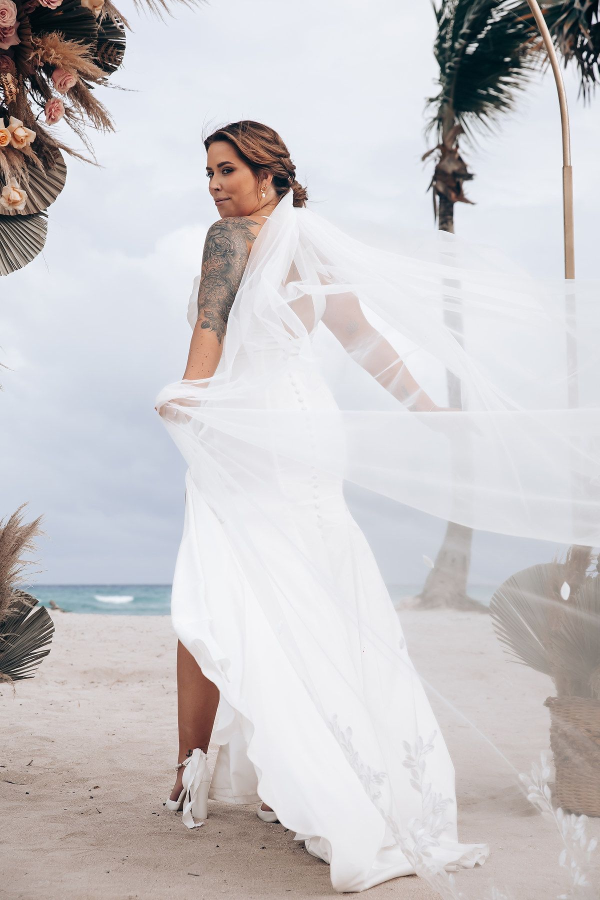 A flowing white wedding dress catches the ocean breeze on a tropical beach.