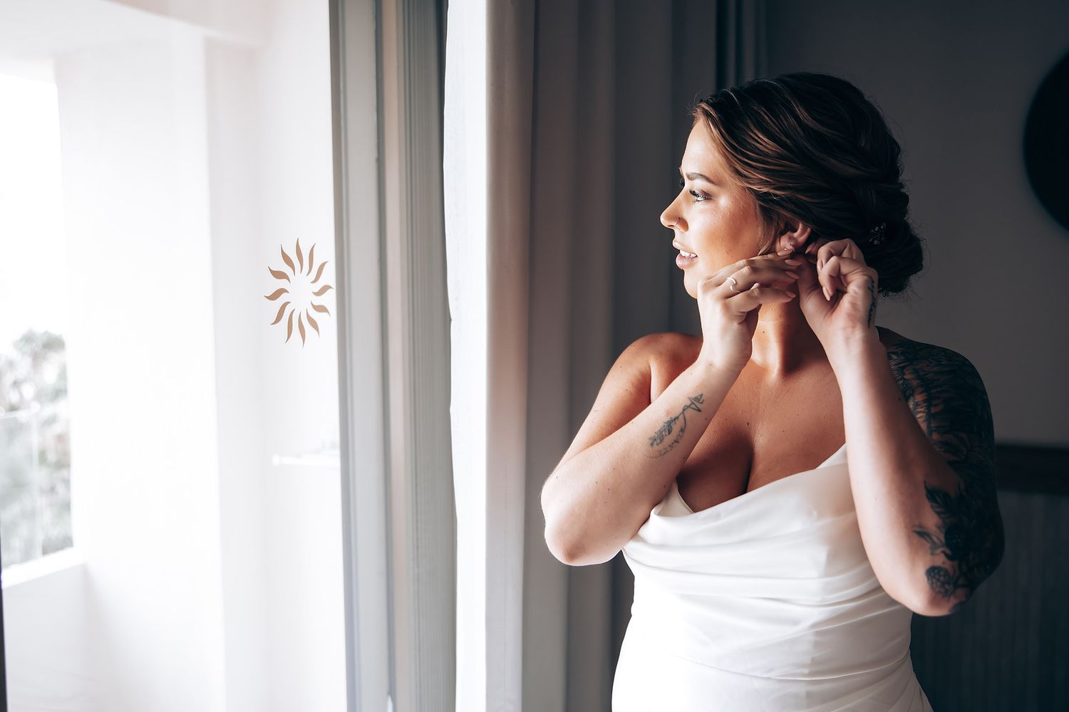 Elegant bridal preparation scene by window with flowing white dress and natural light.