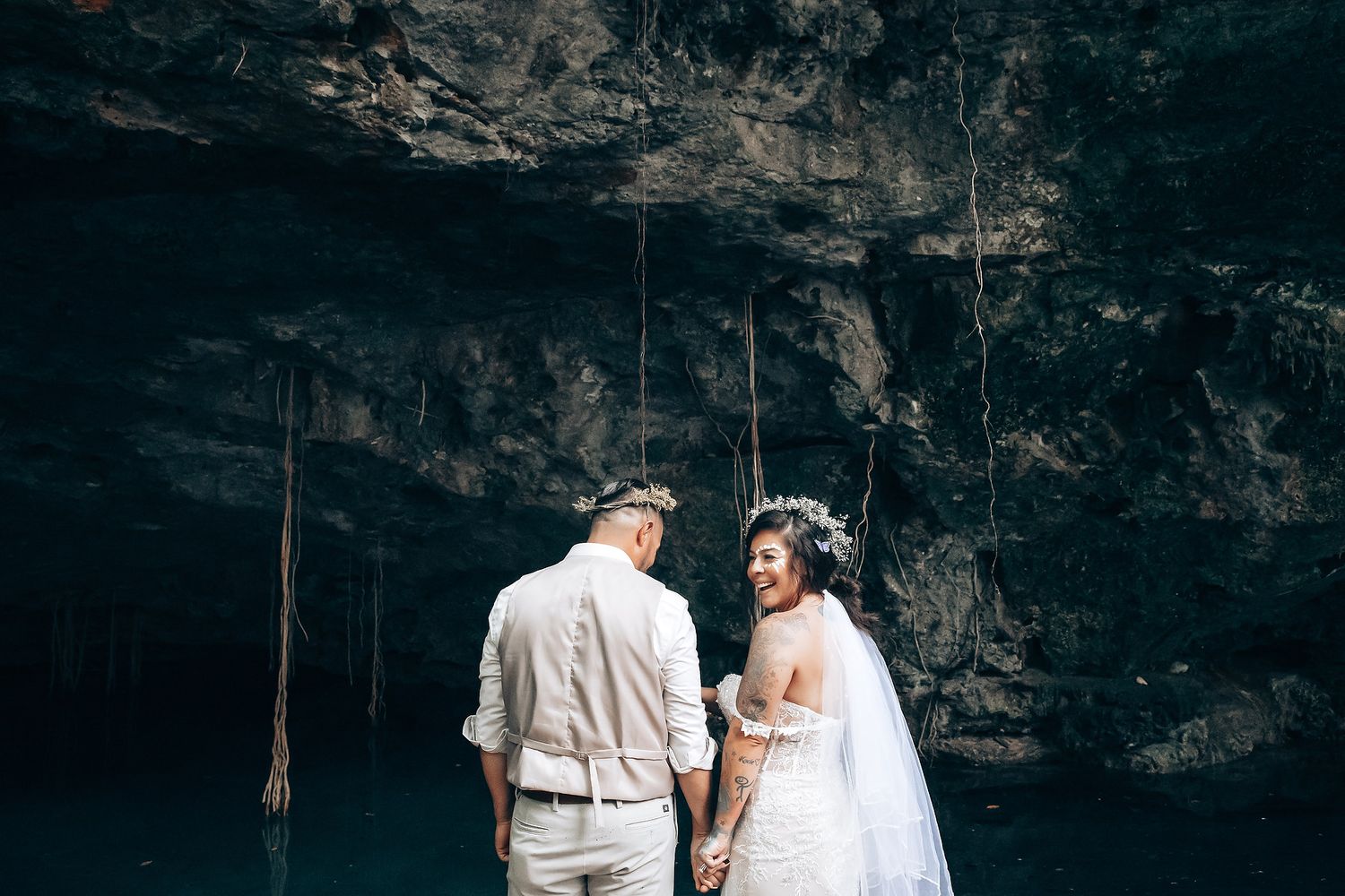 Wedding ceremony takes place under a dramatic rocky overhang or cave entrance.
