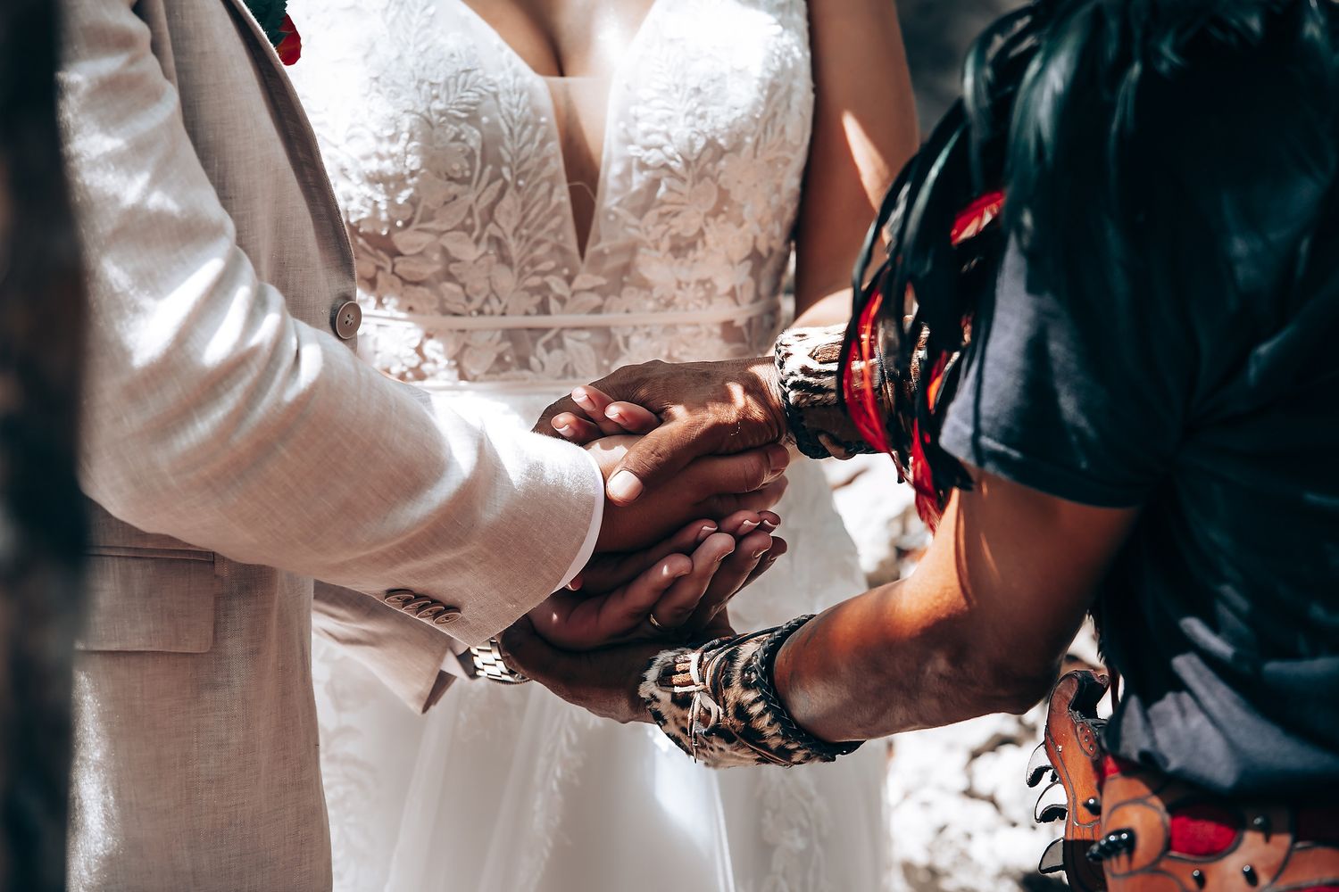 Close-up details of wedding ceremony hands and flowers against white attire.