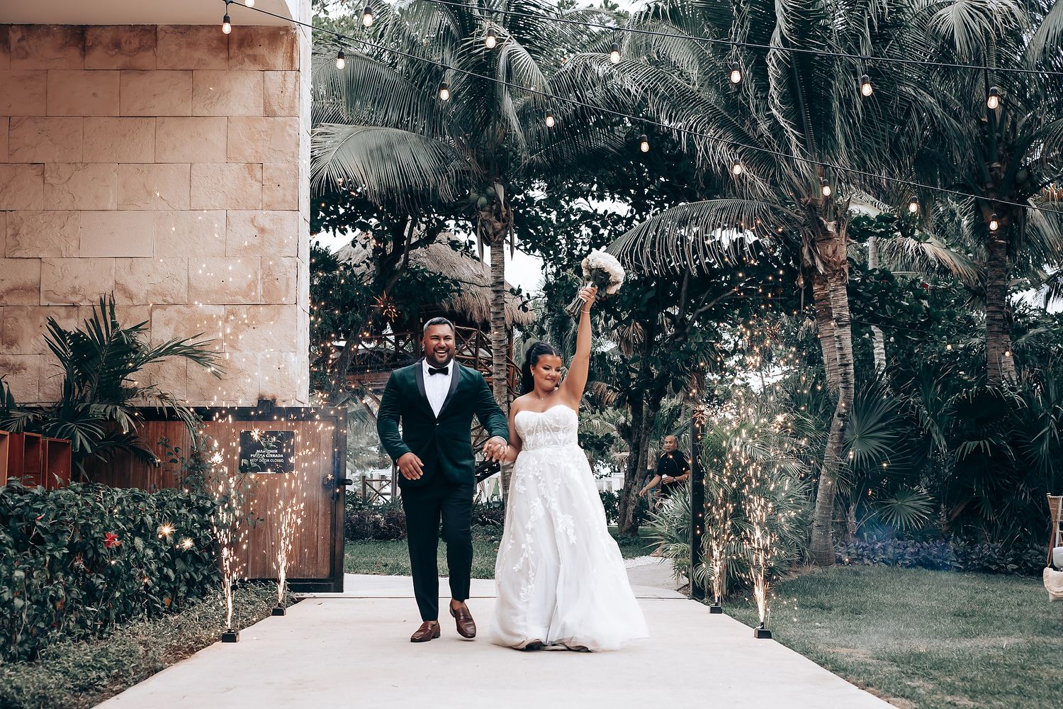 Wedding couple poses together against a brick wall backdrop in an outdoor garden setting.