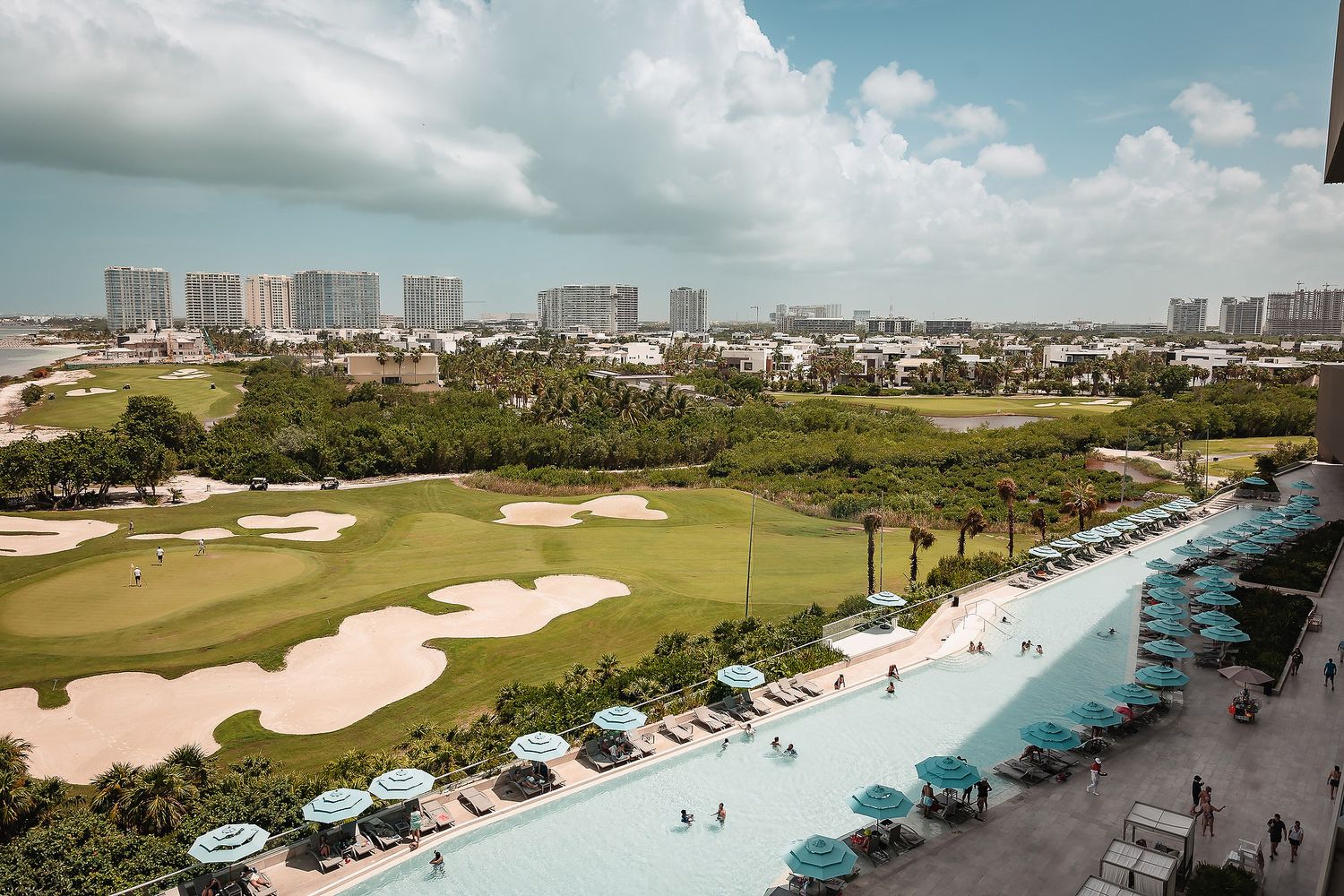 Aerial panoramic view of a coastal resort area with golf courses and beachfront buildings.