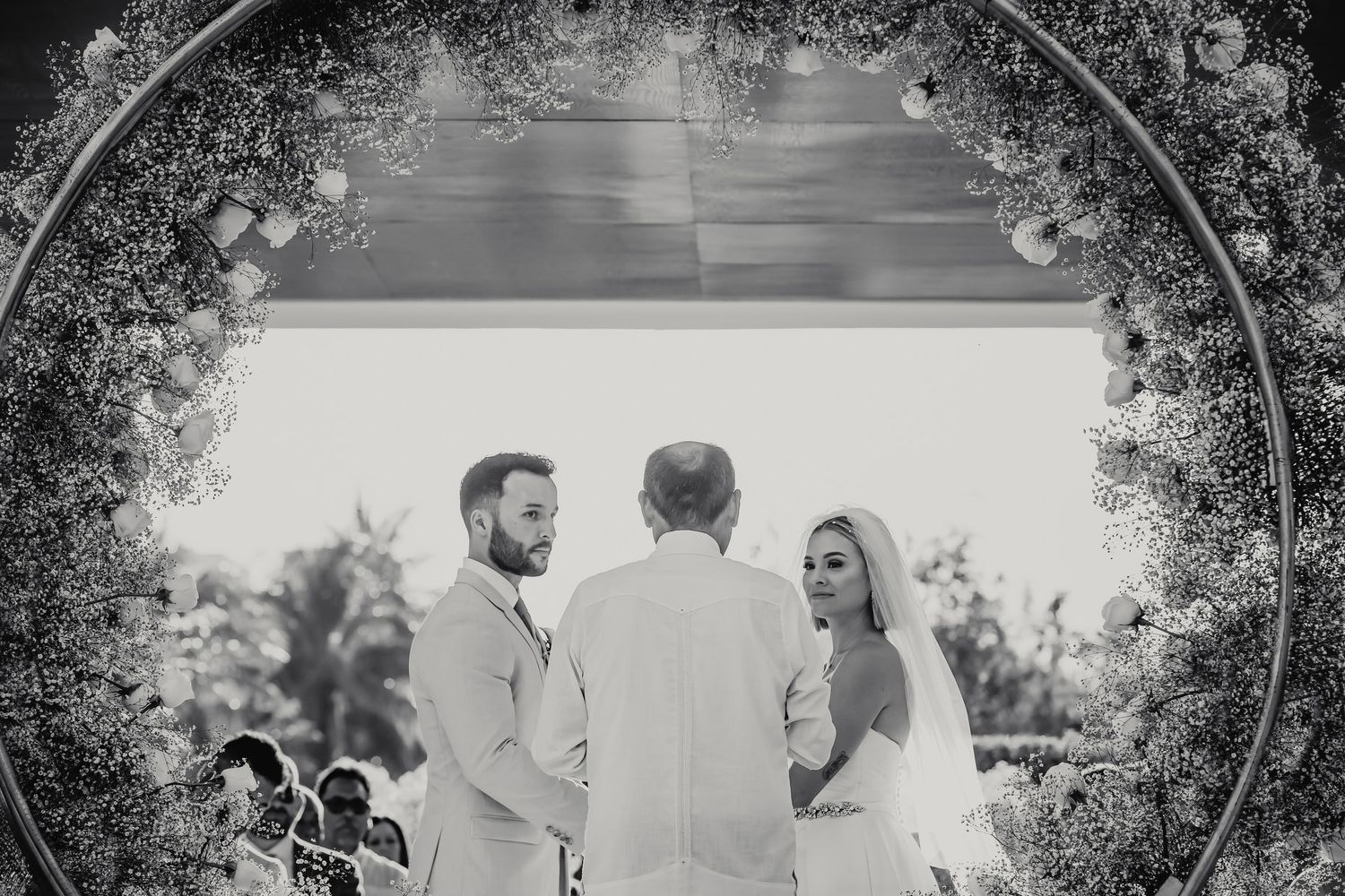 Black and white photo of bride and groom at altar framed by circular floral wedding arch.