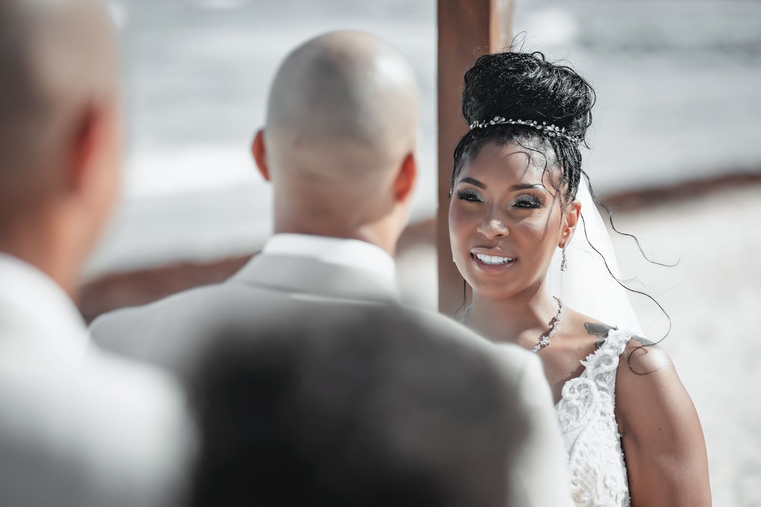 A smiling bride in a white lace gown gazes at her groom during an intimate wedding ceremony.