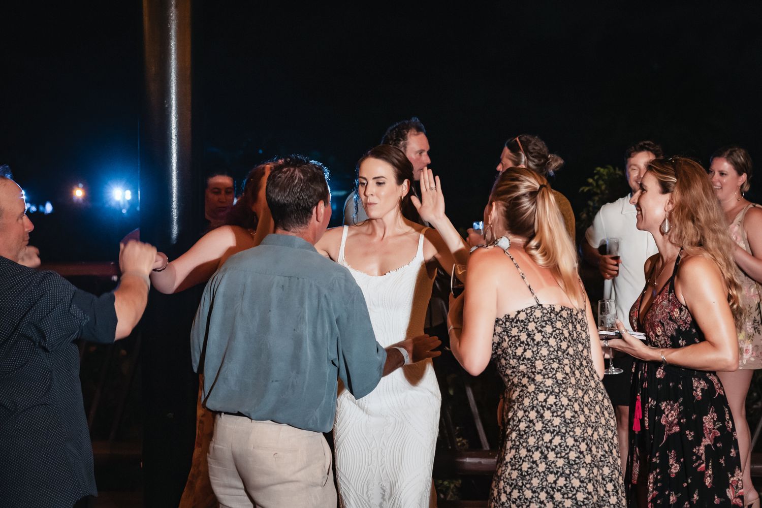 Bride in white dress dancing with guests at an outdoor evening wedding reception celebration.