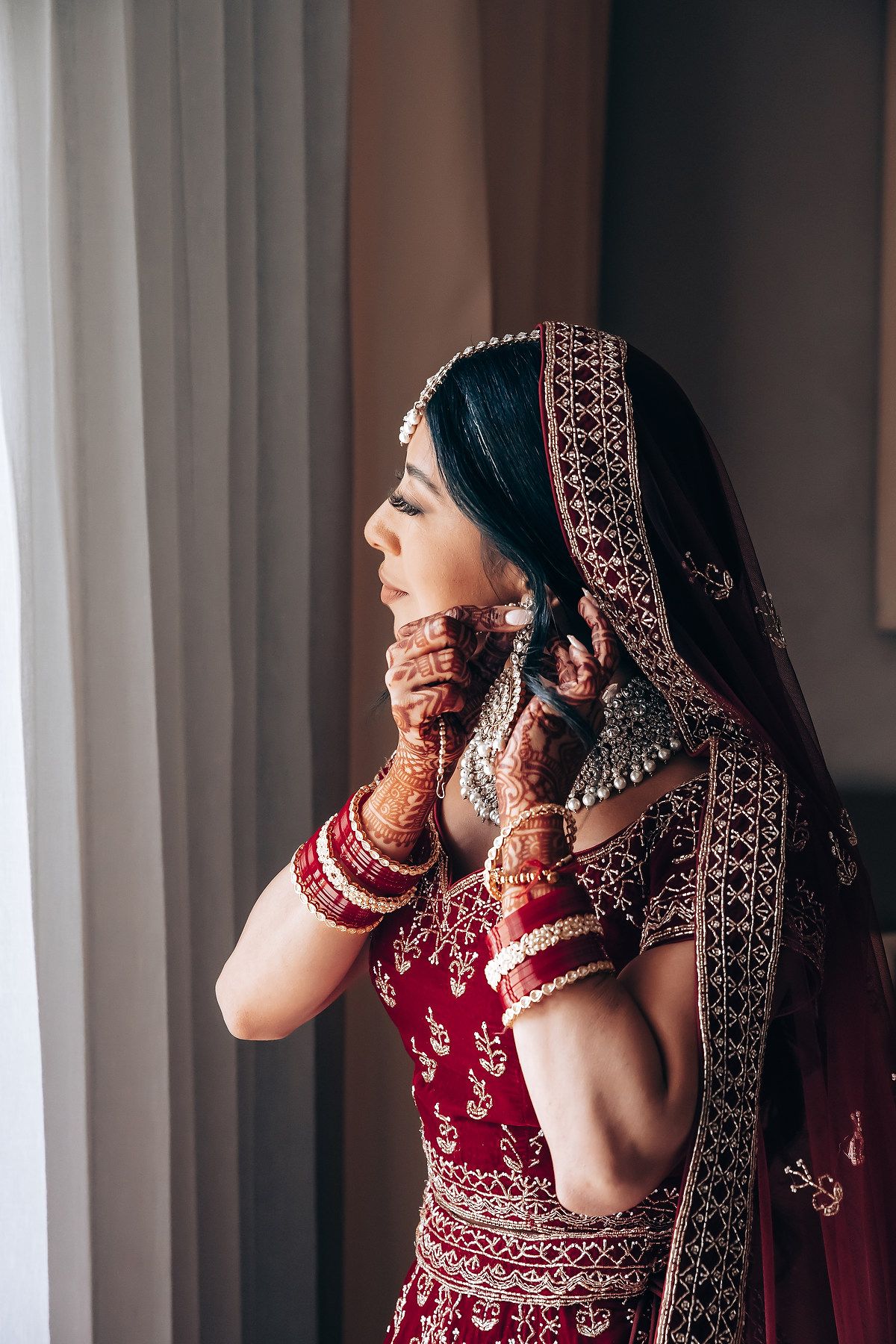 Side view of bride in traditional red lehenga with intricate embroidery and henna-adorned hands.