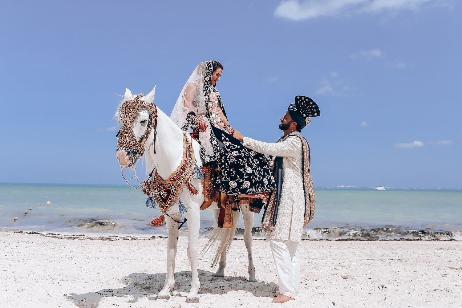 White horse walks along pristine beach with turquoise water in background.