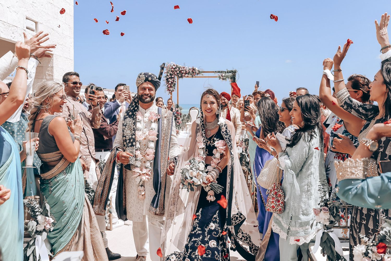 Celebration scene with guests throwing flower petals under a blue sky.