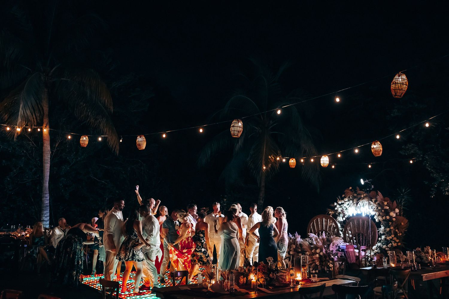Outdoor evening celebration with string lights and dancing silhouettes against dark sky.